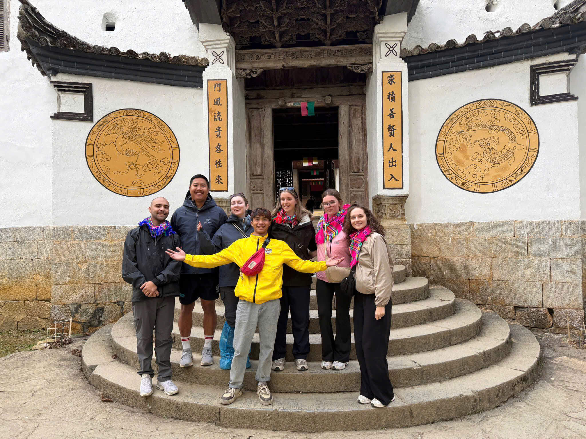 A group of diverse travelers posing in front of the historic Hmong King's Palace (Dinh Vua Meo) during a 4-day Ha Giang Loop tour in Vietnam.