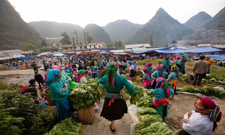 Crowded morning market in Ha Giang where various ethnic groups in colorful traditional headscarves trade fresh vegetables and goods.