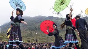 Young women in colorful traditional costumes performing a synchronized umbrella dance against a misty mountain backdrop in Ha Giang.