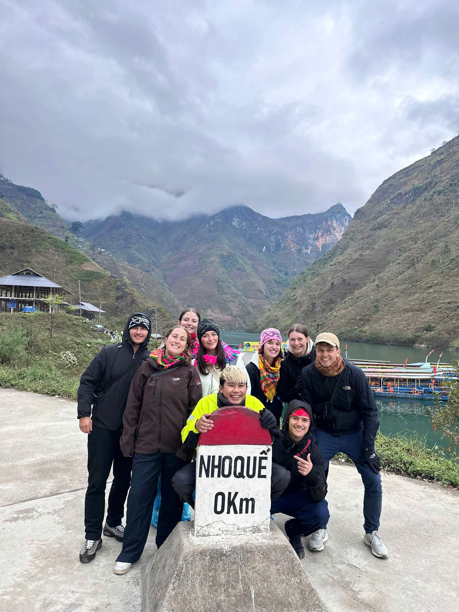 Travelers taking a group photo at the Nho Que 0km milestone before taking a scenic boat ride through Tu San Canyon on their Ha Giang loop.
