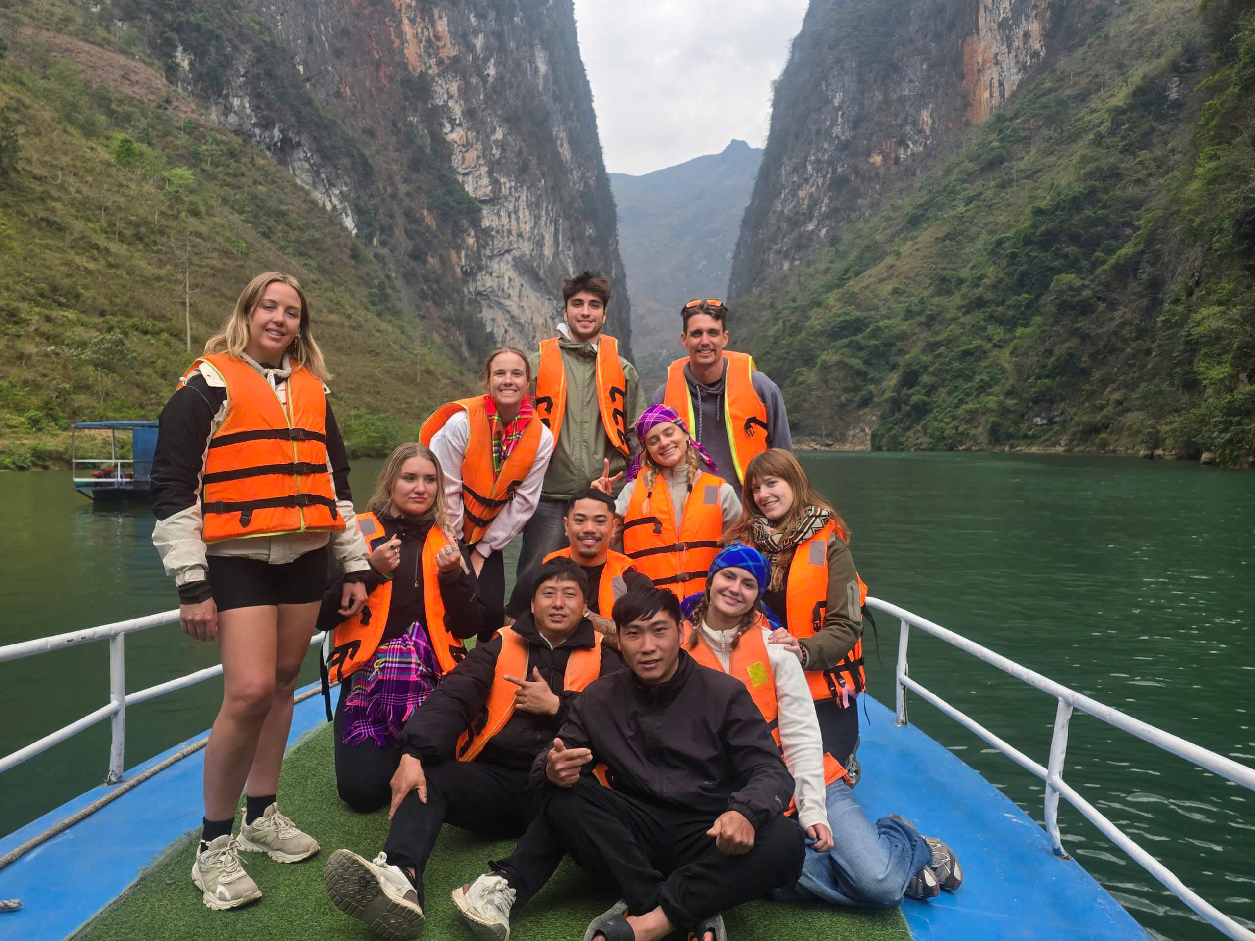 Group of tourists and guides wearing life jackets enjoying a boat trip on the Nho Que River through Tu San Canyon