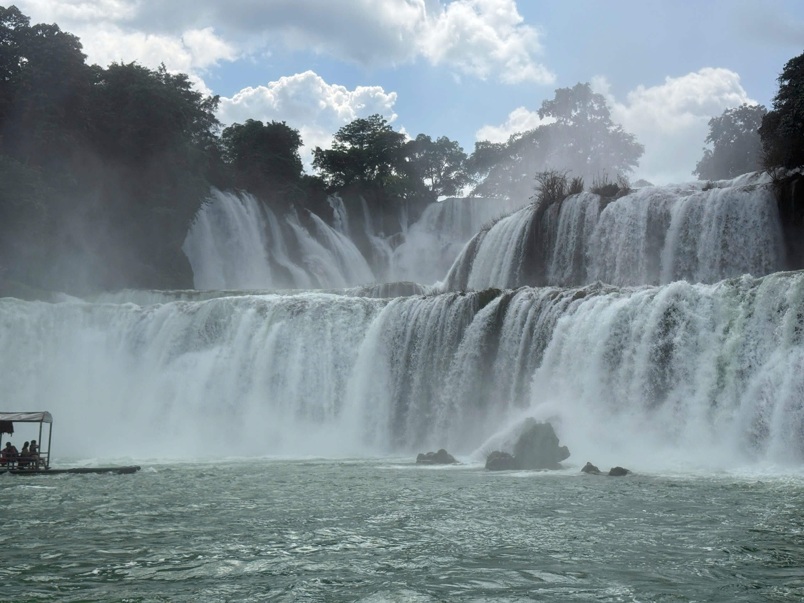 Majestic view of the cascading Ban Gioc Waterfall with a traditional bamboo raft on the Cao Bang Loop.