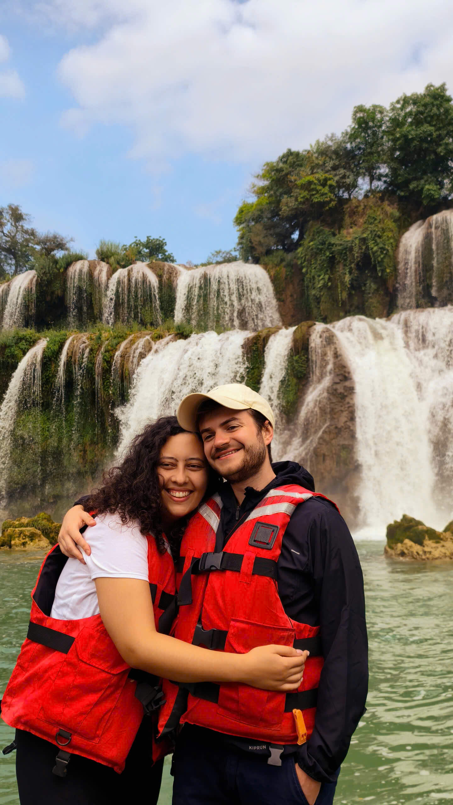 Excited travelers with open arms experiencing the powerful mist of Ban Gioc Waterfall on a raft.