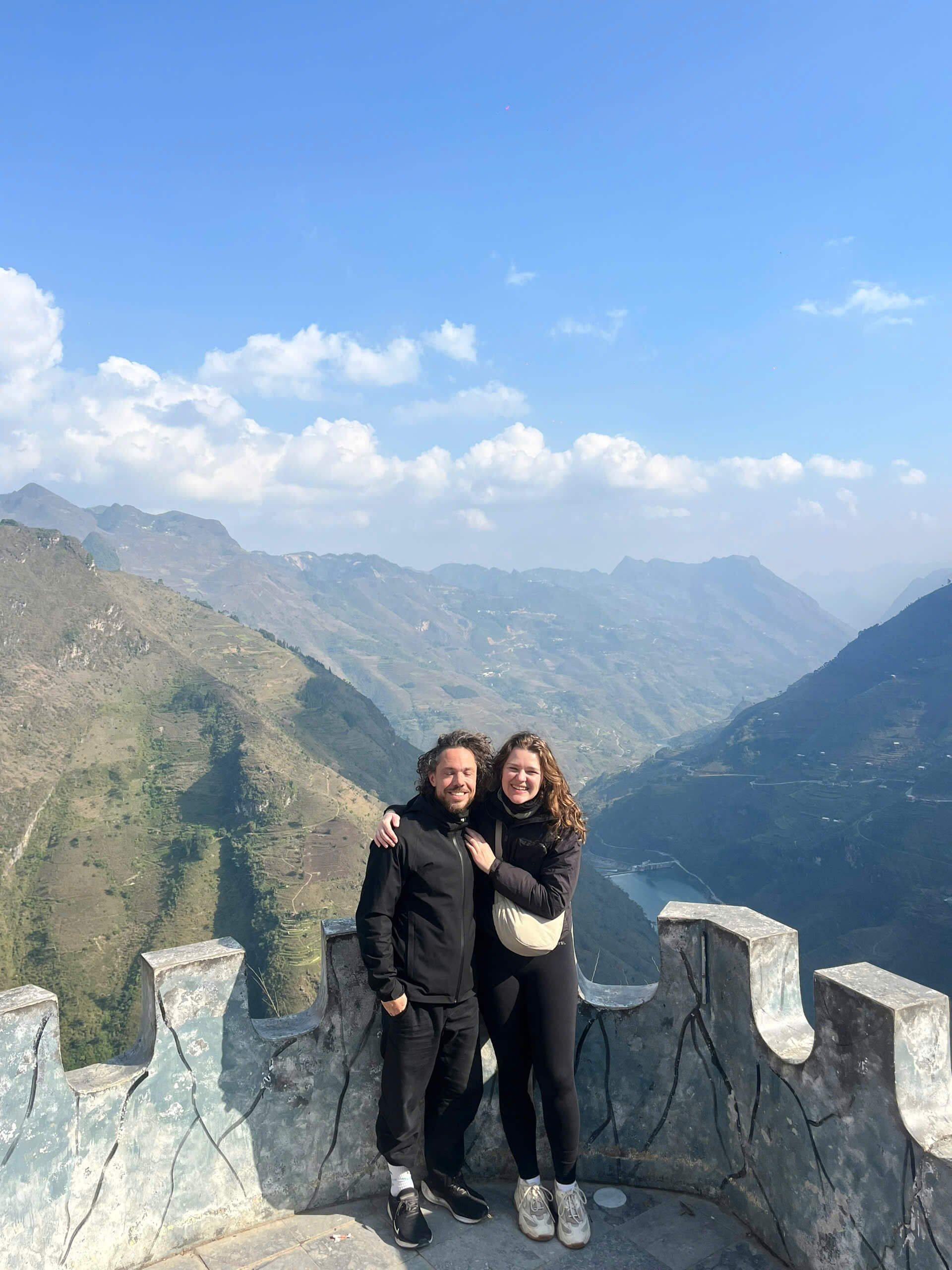 A romantic couple kissing at the famous stone viewpoint overlooking the deep, majestic canyon of the Ma Pi Leng Pass on the Ha Giang Loop.
