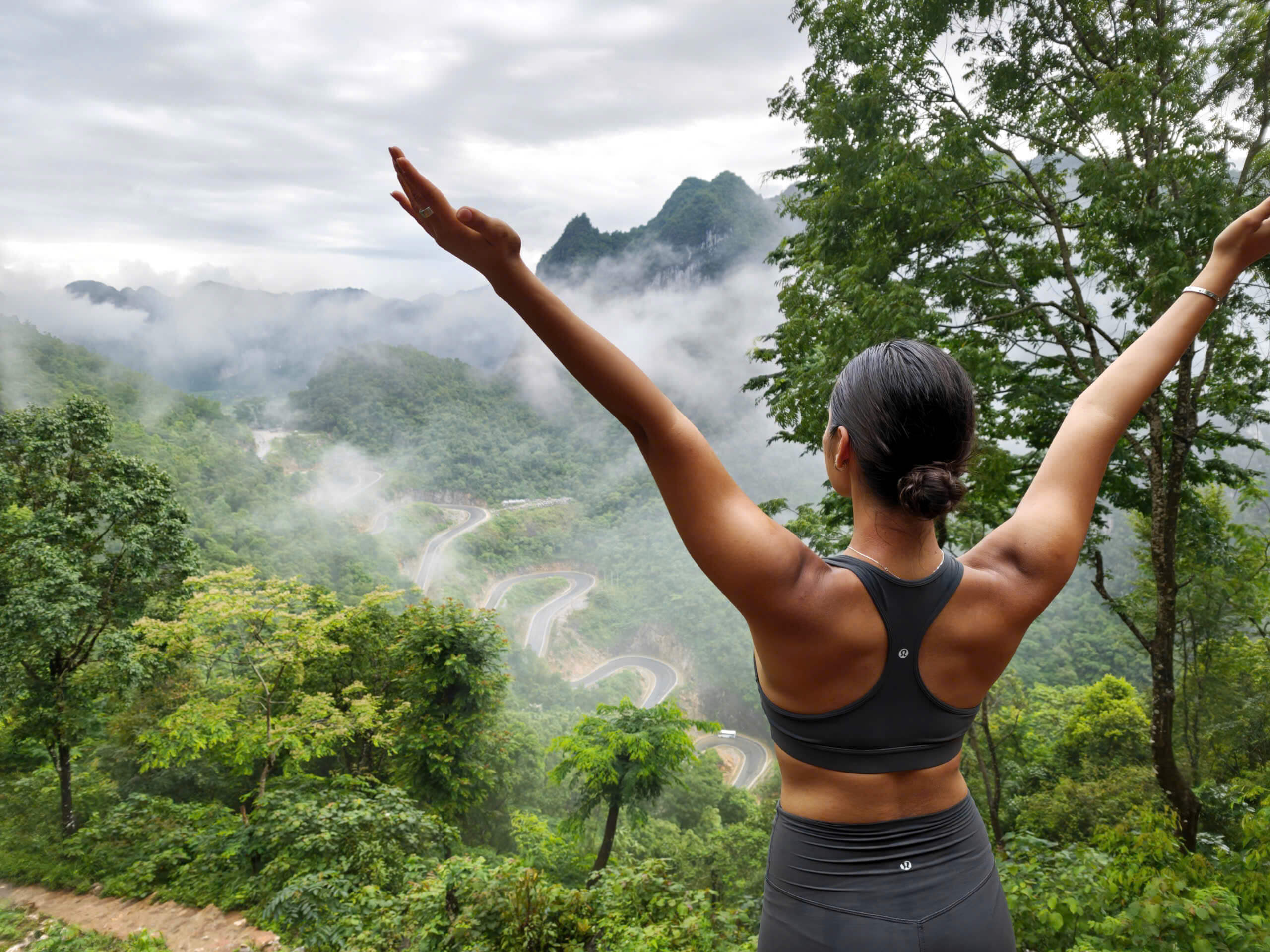 A group of travelers and their local guide smiling and posing on a rugged rocky cliff edge, high above the iconic winding 14-level Me Pia Pass in Cao Bang.