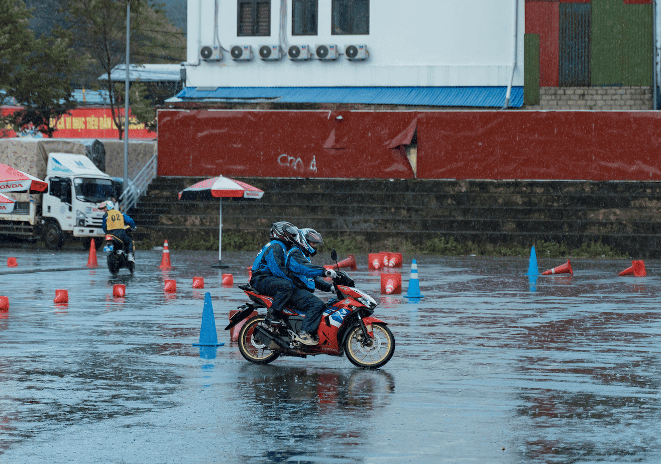 A Motorventures guide in a blue raincoat and helmet practices tight cornering and skid control on a black Honda motorcycle during a heavy rainstorm.