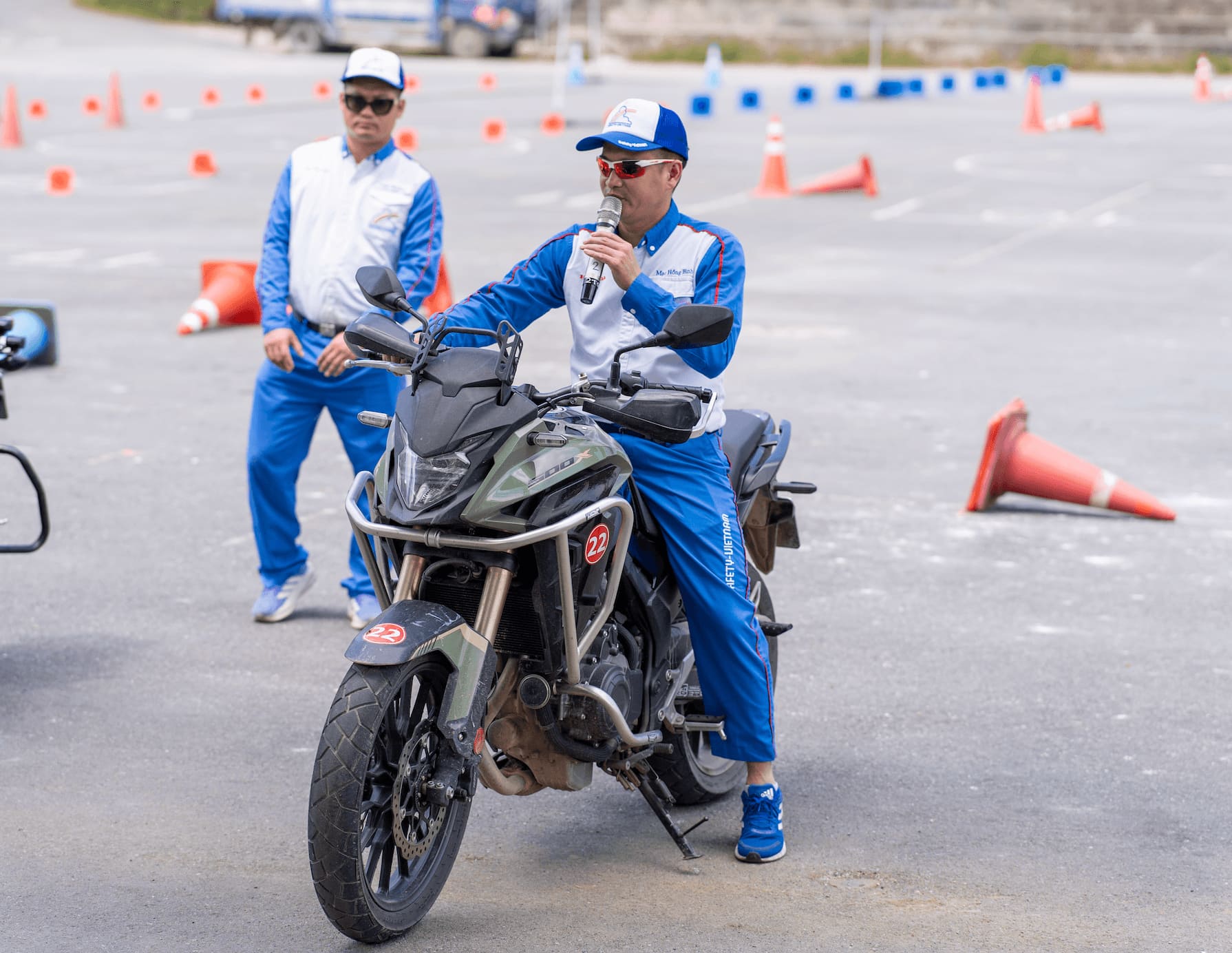 A Honda Vietnam master instructor sitting on a large adventure motorcycle speaks into a microphone, explaining advanced riding techniques to the Motorventures team on a training course.