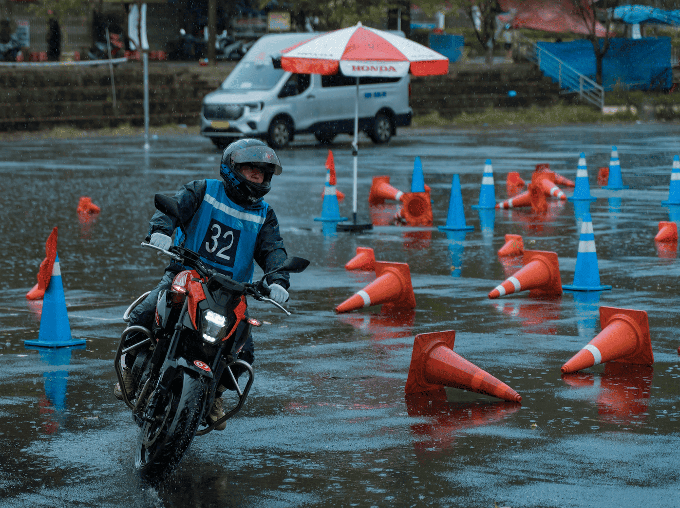 Motorventures guides wearing full blue rain gear navigate a red motorcycle with a passenger through an orange cone course during heavy rain training.
