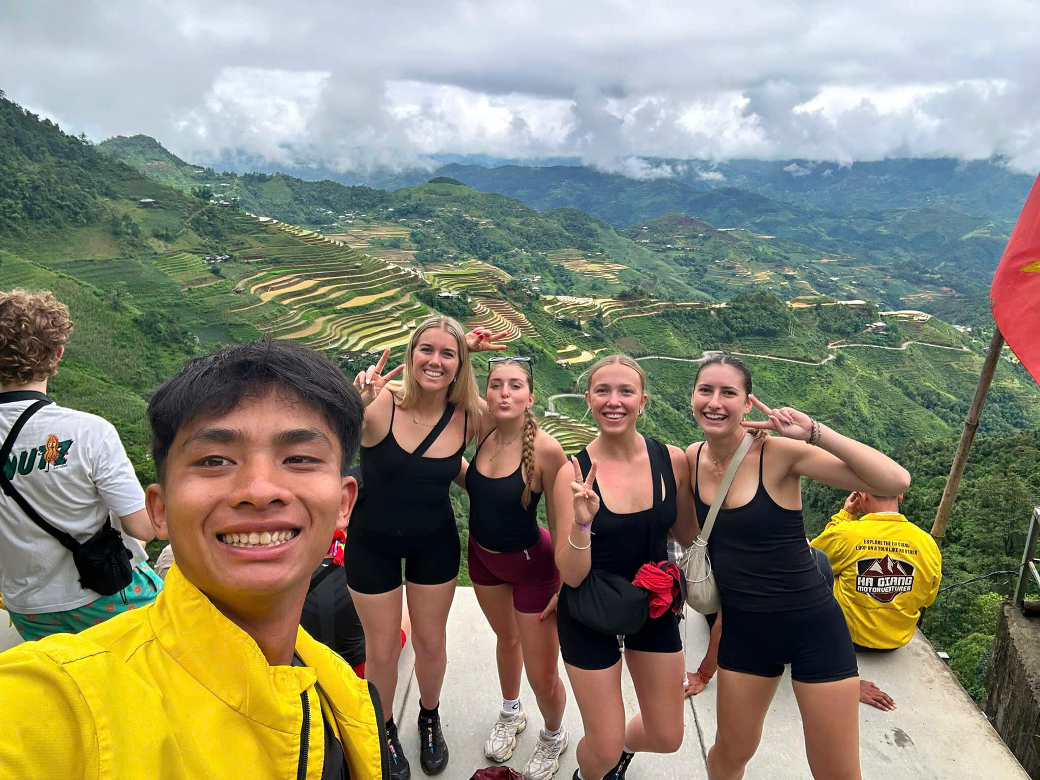 A Motorventures guide taking a group selfie with four female tourists overlooking spectacular, vibrant green rice terraces and misty mountains in Northern Vietnam.