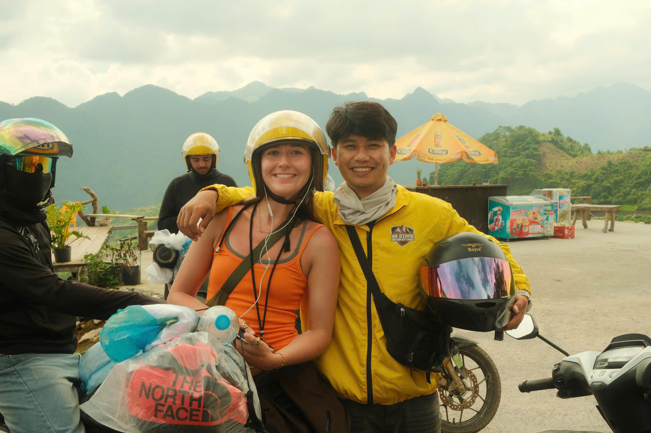 A smiling female tourist posing with her Motorventures Easy Rider guide on a motorbike, showcasing her luggage securely strapped and wrapped in a waterproof bag behind them.