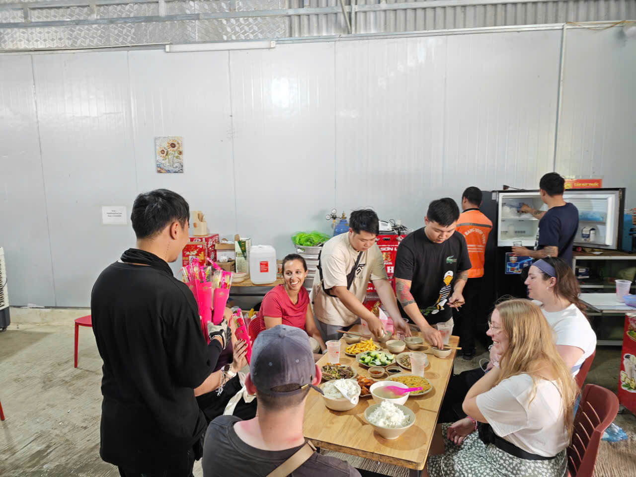 A smiling Vietnamese Easy Rider guide handing a single red rose to a happy female tourist during a group dinner at a local restaurant on the Ha Giang loop.