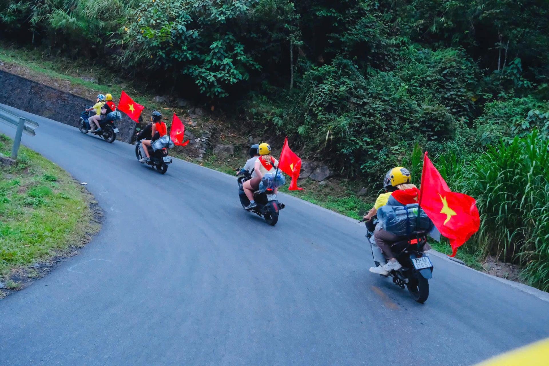 A close up of a tourist riding on the back of an easy rider motorbike with luggage securely strapped and a large red star flag waving during a road trip.